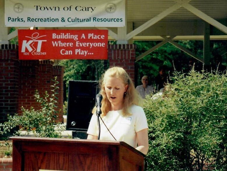 Alice Webb speaking at a podium in front of a banner that reads 